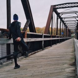 L'image représente un coureur sur un pont, e train de faire des étirements dans le but de prévenir les courbatures. Comment soigner une courbature musculaire avec les huiles essentielles