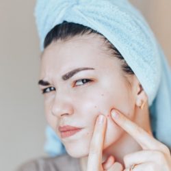 L'image représente une ado devant la glace en train de presser un de ses boutons.
