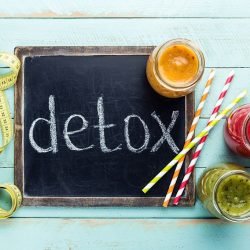 Ardoise avec l’inscription « detox » entourée de jus détox colorés et d’un mètre ruban, illustrant une cure de purification du foie et du corps.