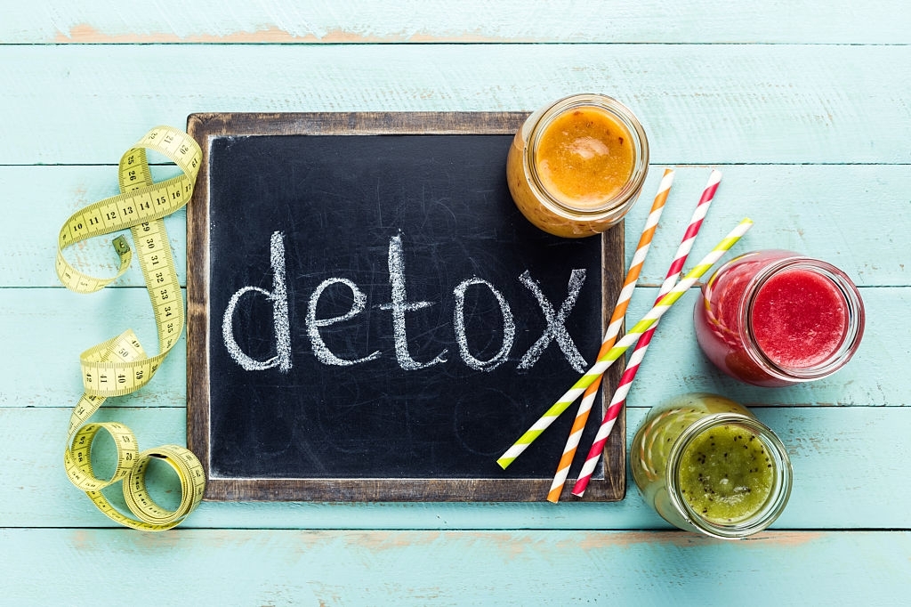Ardoise avec l’inscription « detox » entourée de jus détox colorés et d’un mètre ruban, illustrant une cure de purification du foie et du corps.