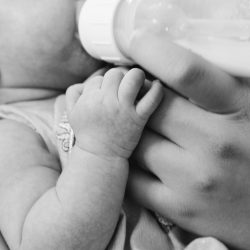 Nourrisson buvant un biberon, tenu dans les bras d’un adulte – Alimentation et reflux gastro-œsophagien