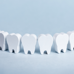 L'image représente une rangée de dents blanches stylisées, alignées côte à côte contre un fond bleu clair. Ces dents en forme de symbole ou jouet évoquent la croissance des dents chez un enfant, un sujet pertinent pour discuter des moyens de soulager la poussée dentaire chez les bébés. Cela pourrait symboliser la santé dentaire, le développement des jeunes enfants ou la dentisterie pédiatrique.