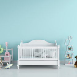 Image d'une chambre d'enfant paisible et minimaliste avec un mur d'un bleu pastel doux. Au centre, un berceau blanc classique avec des draps blancs évoque une atmosphère de calme et de sécurité pour le nourrisson. Sur la gauche, une étagère en forme de cactus et une guitare rose miniature suggèrent une ambiance ludique et créative. À droite, des blocs de construction avec des lettres alphabétiques et un cadre contenant une illustration de hibou renforcent un environnement éducatif. Un ours en peluche brun et un ballon multicolore sont posés sur le sol, ajoutant une touche de confort et d'invitation au jeu. L'ensemble crée une atmosphère sereine qui peut contribuer à l'apaisement des coliques du nourrisson grâce à un environnement stable et réconfortant.