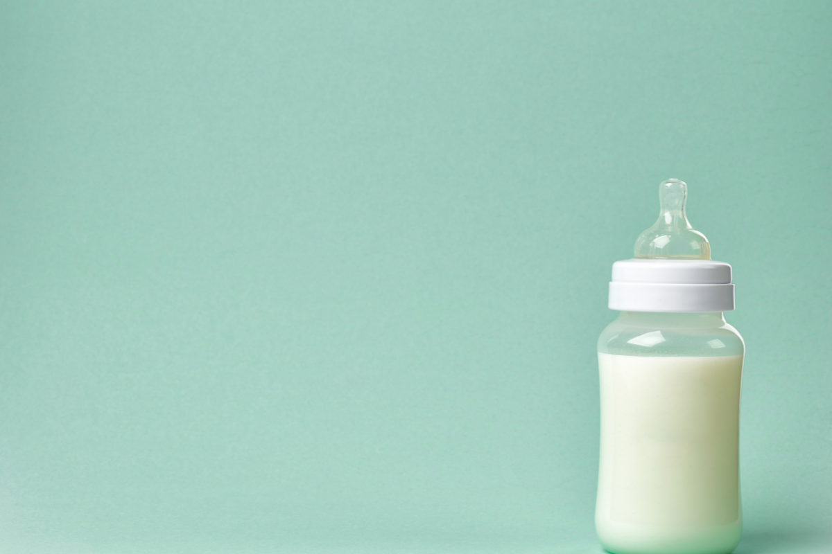 Un biberon rempli de lait avec une tétine ronde en silicone posé sur un fond uni de couleur vert pastel, évoquant la douceur et la simplicité de l'alimentation infantile.