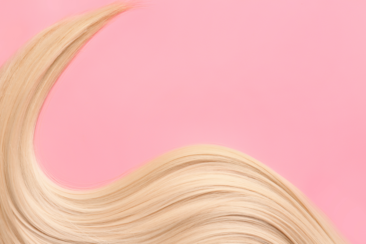 Mèche de cheveux blonds ondulés sur fond rose, symbolisant la santé et la beauté capillaire.