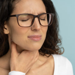 L'image représente une femme qui a visiblement un problème de gorge, de voix. elle a la main sur la gorge. aphonie et enrouement de la voix