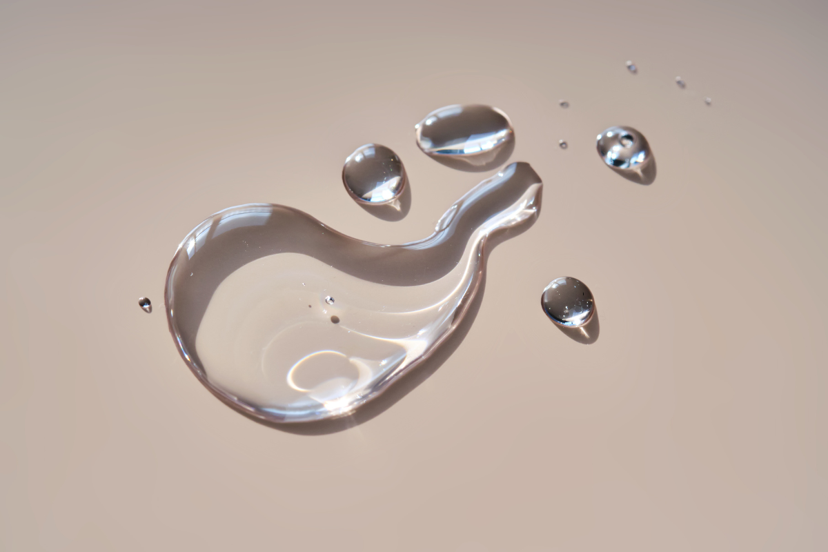Gouttes de sérum hydratant sur une surface beige, capturant la lumière pour illustrer l’efficacité d’un soin visage nourrissant.