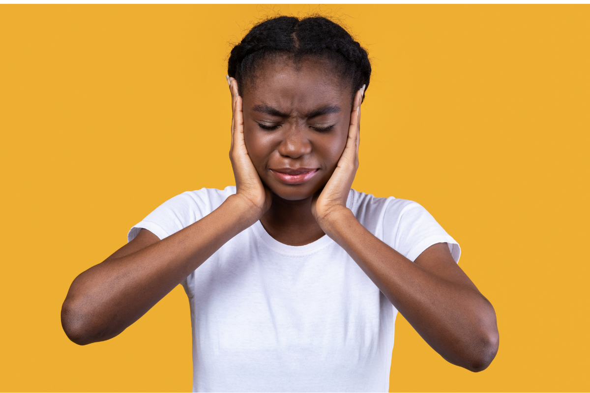 Femme se tenant les oreilles, exprimant la douleur ou l'inconfort.