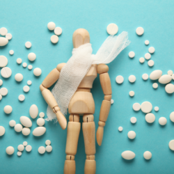 l'image représente un pantin en bois avec une écharpe autour de la gorge. Il y a également plein de remèdes et granules homéopathiques autour de lui