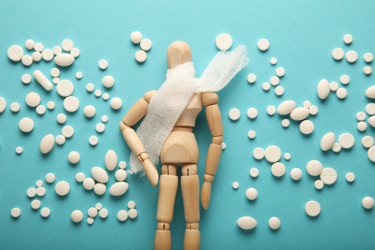 l'image représente un pantin en bois avec une écharpe autour de la gorge. Il y a également plein de remèdes et granules homéopathiques autour de lui