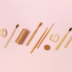 Zero-Waste-Accessoires für ein umweltfreundliches Badezimmer: Zahnbürsten aus Bambus, natürliche Loofahs und kompostierbare Etuis auf rosafarbenem Hintergrund.