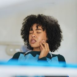 L'image représente une personne qui se tient la joue en faisant la grimace. Elle a probablement des douleurs dentaires. Stomatologie