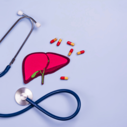 Cette image montre un stéthoscope bleu marine et une représentation schématique d'un foie en couleur rose vif, avec plusieurs gélules disposées autour. Le fond est de couleur bleu clair, évoquant un environnement médical calme et serein.