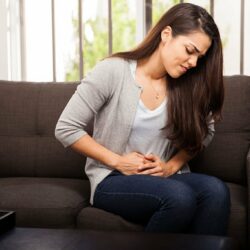 coliques néphrétiques. Une femme sur son canapé, qui a visiblement des douleurs au niveau du ventre