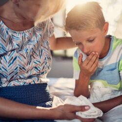 La photo représente un enfant dans les bras de ses parents. il a l'air d'avoir la nausée, puisqu'il est penché et porte une main à sa bouche