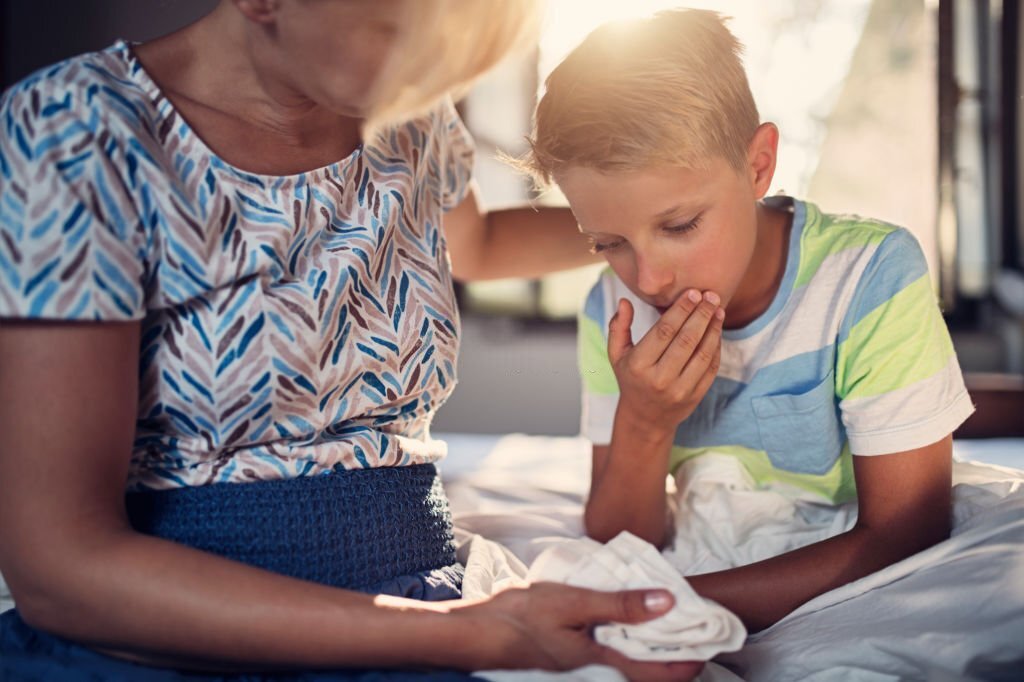 La photo représente un enfant dans les bras de ses parents. il a l'air d'avoir la nausée, puisqu'il est penché et porte une main à sa bouche