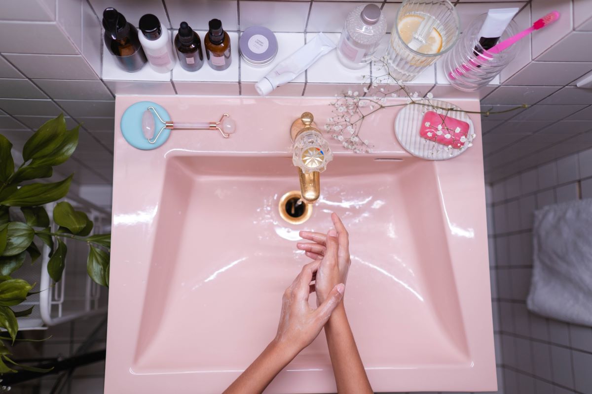 L'image représente une photo vu d'en haut d'un lavabo rose et une personne qui s'apprête à faire sa routine skincare anti-acné. peau tendance acnéique