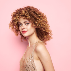 comment prendre soin de mes cheveux bouclés ? L'image représente une femme avec de magnifiques cheveux bouclés, sur un fond rose.