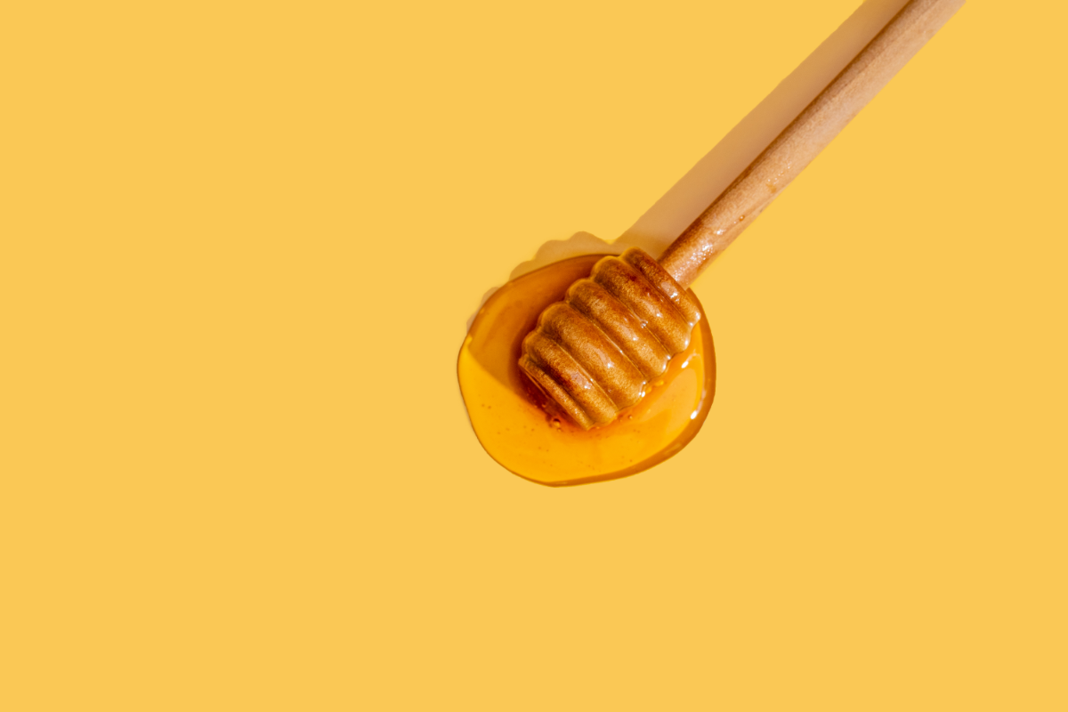 L'image représente une cuillère en bois avec du miel, sur un fond jaune oranger. Les bienfaits du miel de Manuka.