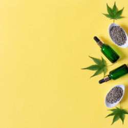 Flacons d’huile de CBD avec des feuilles de chanvre et des graines sur fond jaune, illustrant les nouvelles formes de cannabidiol pour le bien-être.