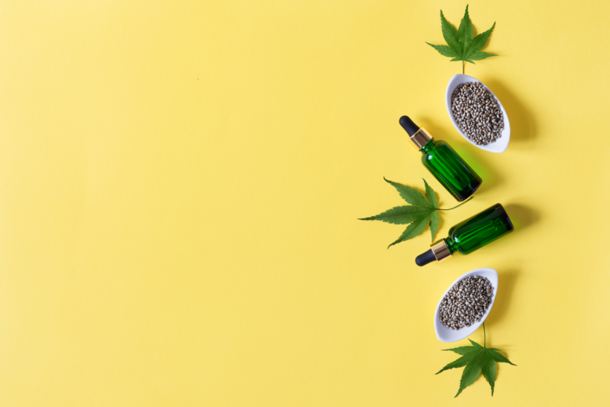 Flacons d’huile de CBD avec des feuilles de chanvre et des graines sur fond jaune, illustrant les nouvelles formes de cannabidiol pour le bien-être.