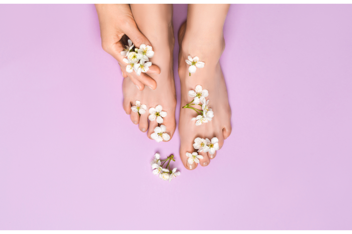 Pieds féminins ornés de fleurs blanches sur fond rose, symbolisant la douceur et l’hydratation après l’utilisation de masques de beauté pour les pieds.