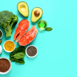 Cette image illustre une sélection d'aliments sains qui pourraient favoriser le développement du tissu adipeux brun, connu pour ses bénéfices métaboliques. Sur un fond turquoise, on trouve du brocoli, des avocats, du saumon, des graines de chia et de lin, des capsules d'huile de poisson, des épinards et des œufs, tous réputés pour leur richesse en acides gras oméga-3 et en nutriments essentiels pour soutenir le métabolisme énergétique et la thermogenèse associés au tissu adipeux brun.