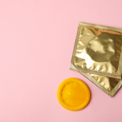 Une enveloppe de préservatif dorée accompagnée d'un préservatif jaune non déroulé sur un fond rose uni. Des aphrodisiaques naturels pour pimenter la Saint Valentin