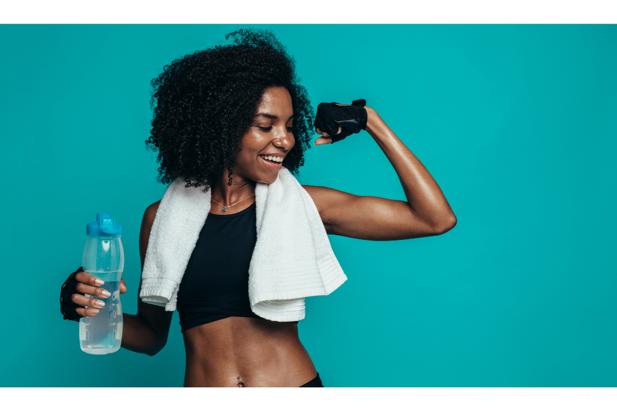 Femme afro-américaine sportive se tenant avec une bouteille d'eau, montrant son biceps et souriant, symbolisant la perte de poids saine et l'hydratation. Combien de temps faut-il pour perdre du poids