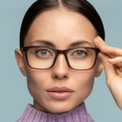Femme tenant délicatement la monture de ses lunettes, révélant un regard attentif et concentré.