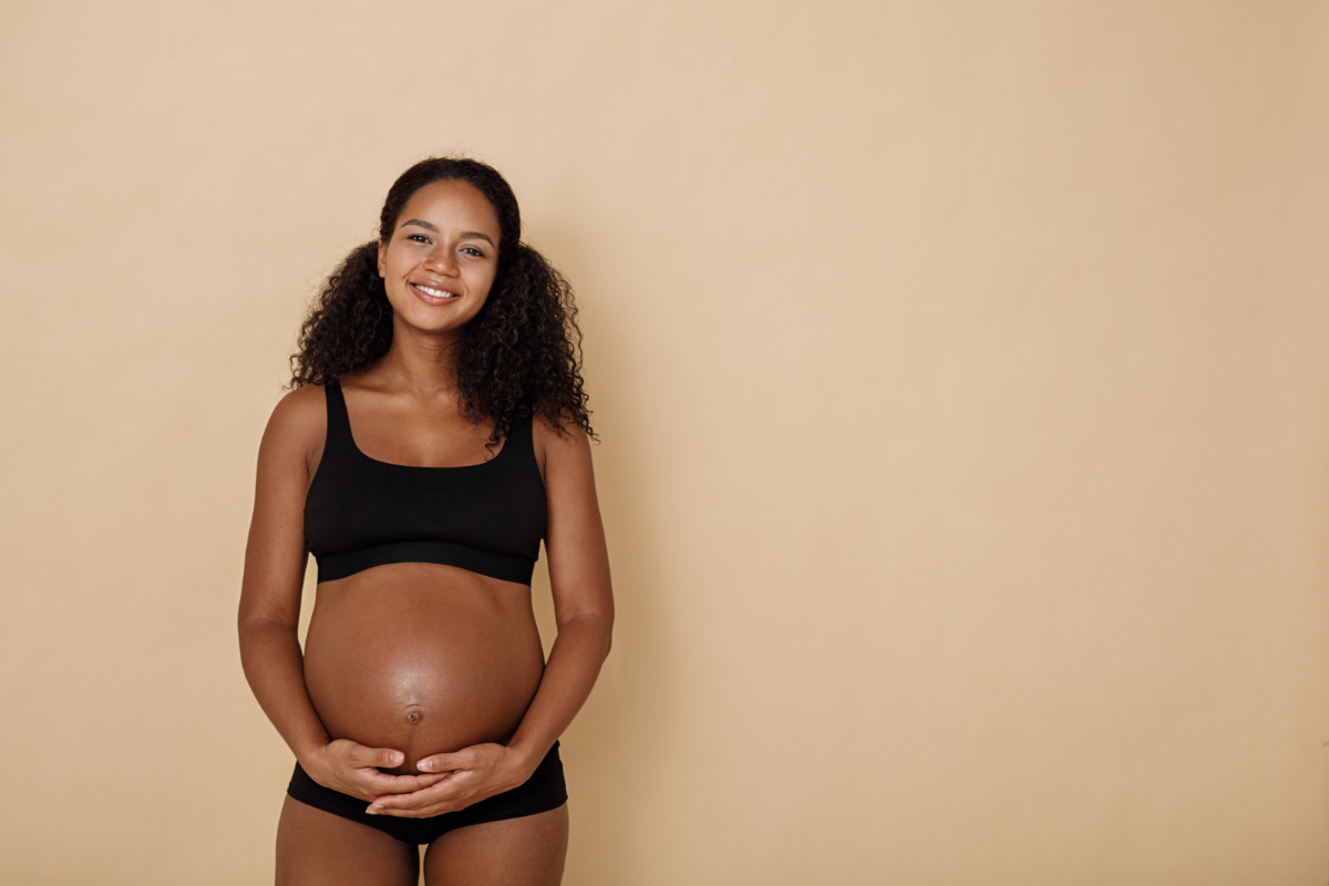 L'image représente une femme enceinte très souriante, qui se tient le ventre. les signes de la grossesse