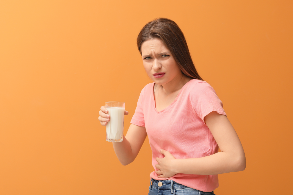 Comment choisir les granules d’homéopathie en cas d’indigestion ? L'image représente une jeune femme tenant un verre de lait, elle se touche le ventre en faisant la grimace pour montrer qu'elle a probablement du mal à digérer.