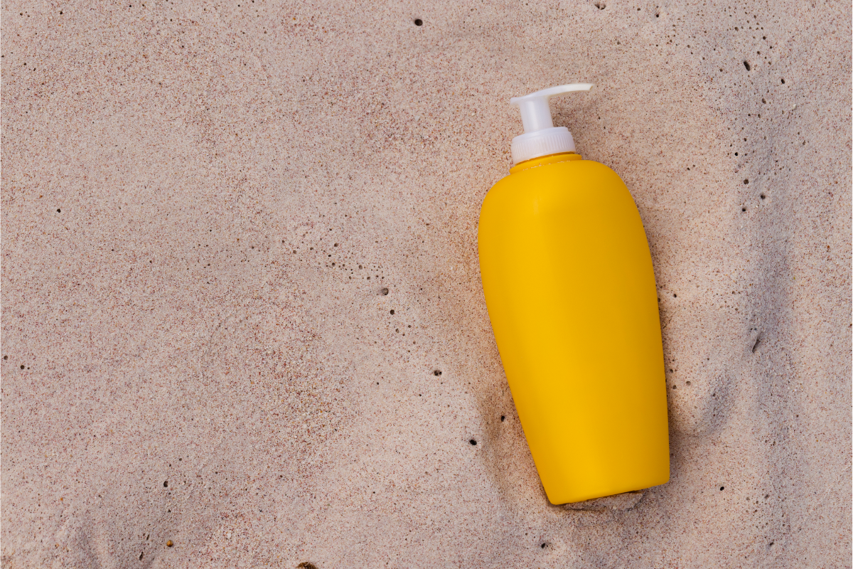 L'image représente un flacon de crème solaire dans le sable