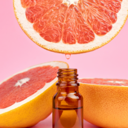 L'image représente une fiole d'huile essentielle et des morceaux de pamplemousses dans le fond pour illustrer le risque intéraction avec le jus de pamplemousse et médicaments