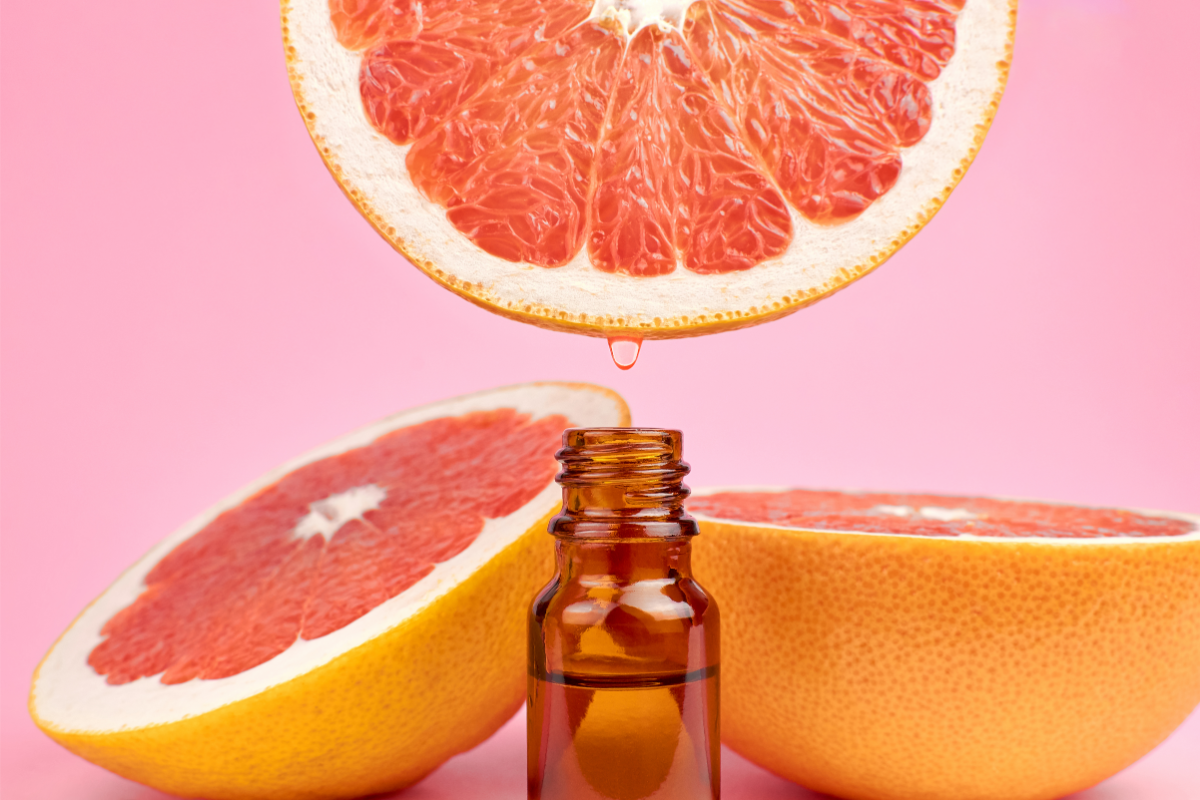 L'image représente une fiole d'huile essentielle et des morceaux de pamplemousses dans le fond pour illustrer le risque intéraction avec le jus de pamplemousse et médicaments