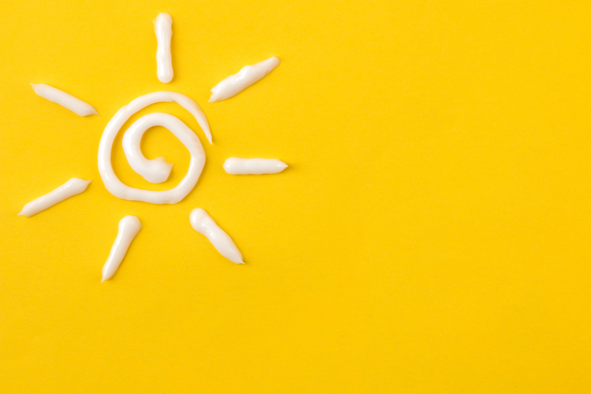 L'image représente un soleil dessiné avec de la crème solaire, sur un fond jaune pour illustrer l'article sur la protection solaire pour les cheveux cheveux