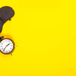 L'image représente un fond jaune vif sur lequel sont posées un réveil ainsi qu'un masque pour dormir pour les yeux. Comment Bien Dormir Lorsqu'il Fait Très Chaud La Nuit. Un bandeau cache yeux et un réveil sur fond jaune