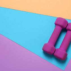 des haltères roses posées sur un tapis coloré pour illustrer le fait de faire du renforcement musculaire pour booster son métabolisme