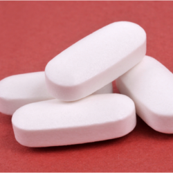 L'image représente des comprimés de Doliprane sur un fond rouge bordeaux. Peut-on utiliser du doliprane pour soulager la douleur sociale ? La réponse dans notre article