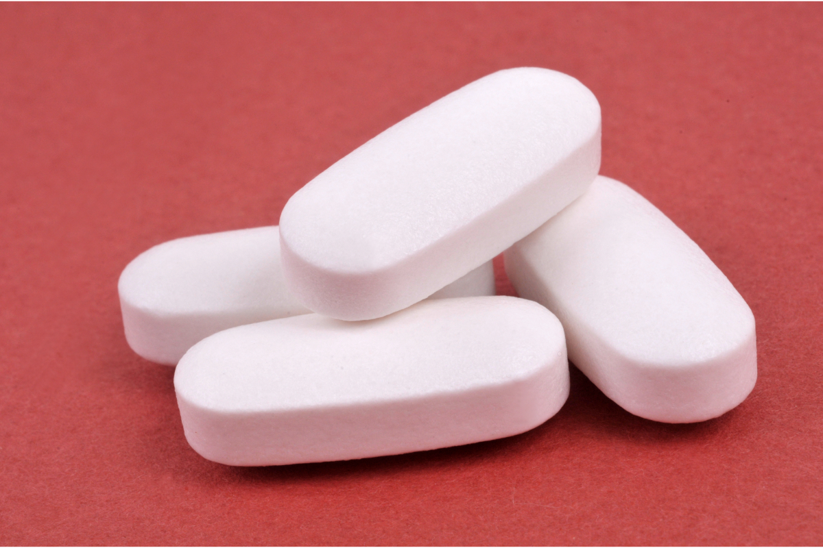 L'image représente des comprimés de Doliprane sur un fond rouge bordeaux. Peut-on utiliser du doliprane pour soulager la douleur sociale ? La réponse dans notre article