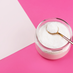 Pot de collagène marin en poudre avec une cuillère dorée, sur un fond rose.