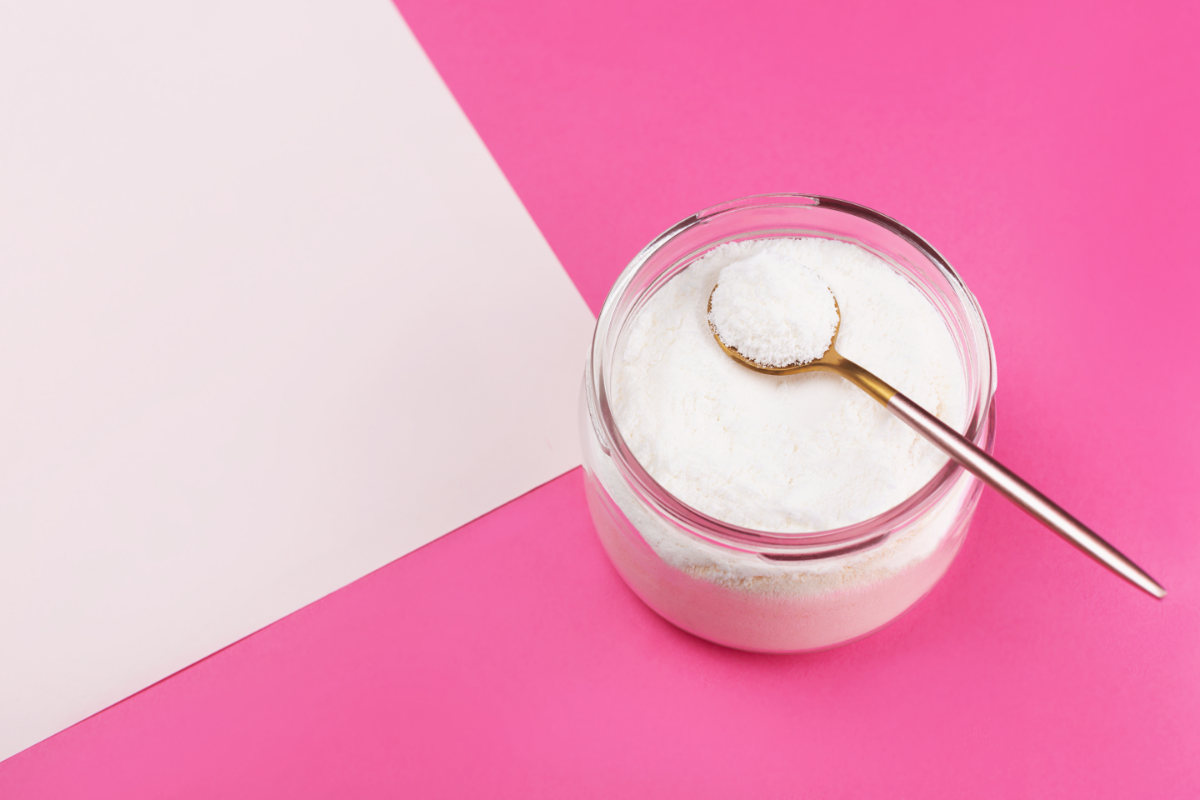 Pot de collagène marin en poudre avec une cuillère dorée, sur un fond rose.