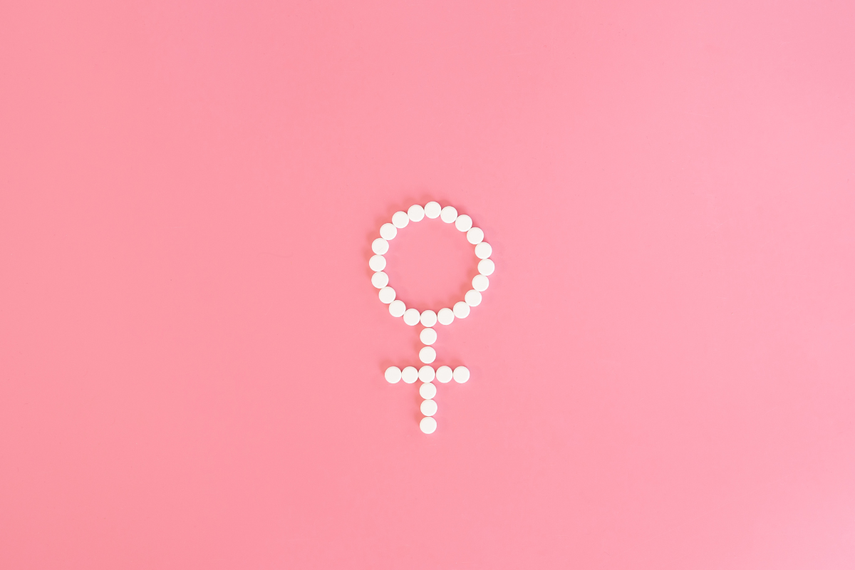 Symbole féminin formé de pilules blanches sur fond rose