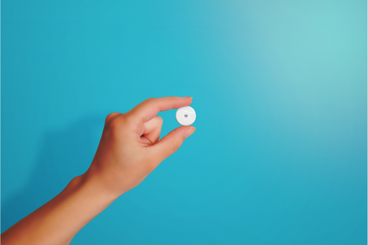 Capteur Freestyle Libre tenu entre les doigts d'une main sur fond bleu.