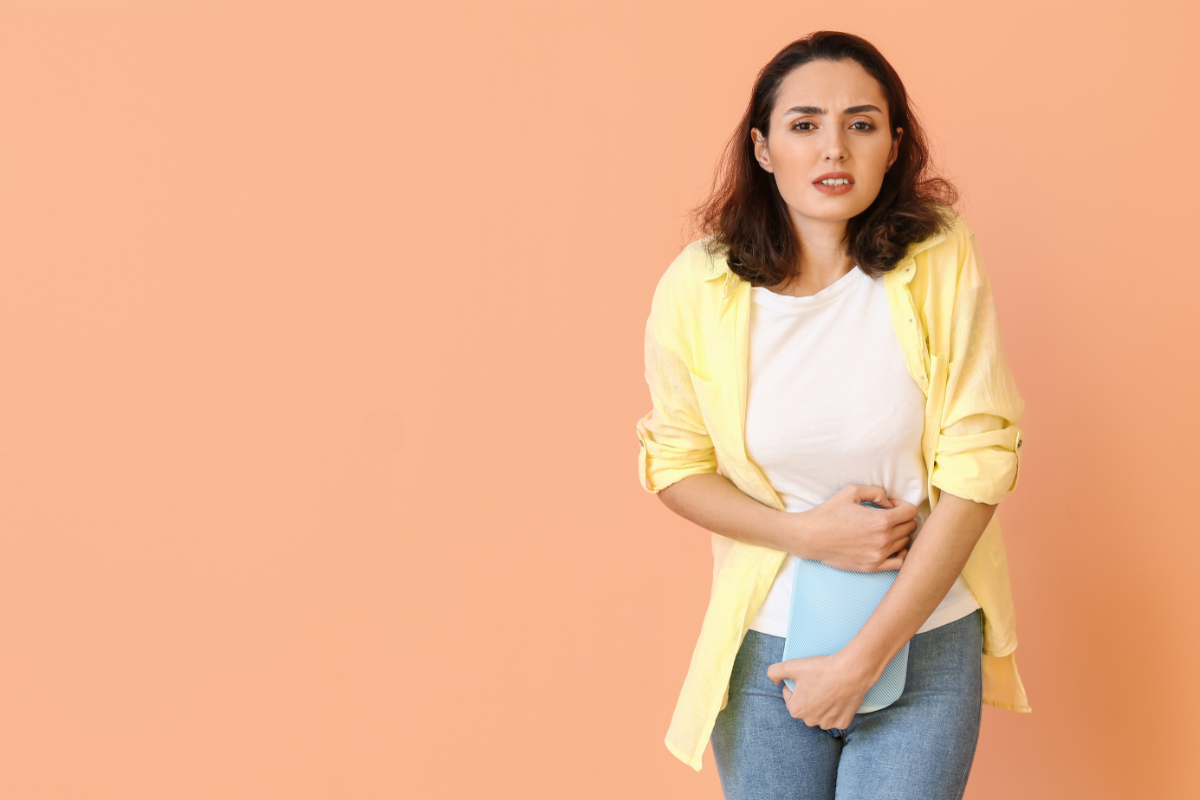 Femme souffrant de douleurs menstruelles, tenant une bouillotte sur son ventre pour soulager ses crampes. Cette image illustre l'importance des remèdes naturels et des pratiques bien-être, comme l'utilisation de la bouillotte, pour soulager les règles douloureuses.