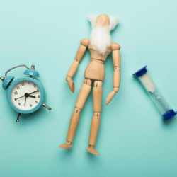 Une horloge, une figurine en bois avec une barbe blanche et un sablier, symbolisant le vieillissement et le temps, illustrant les bienfaits des acides gras C15:0 sur la longévité et la santé cellulaire.