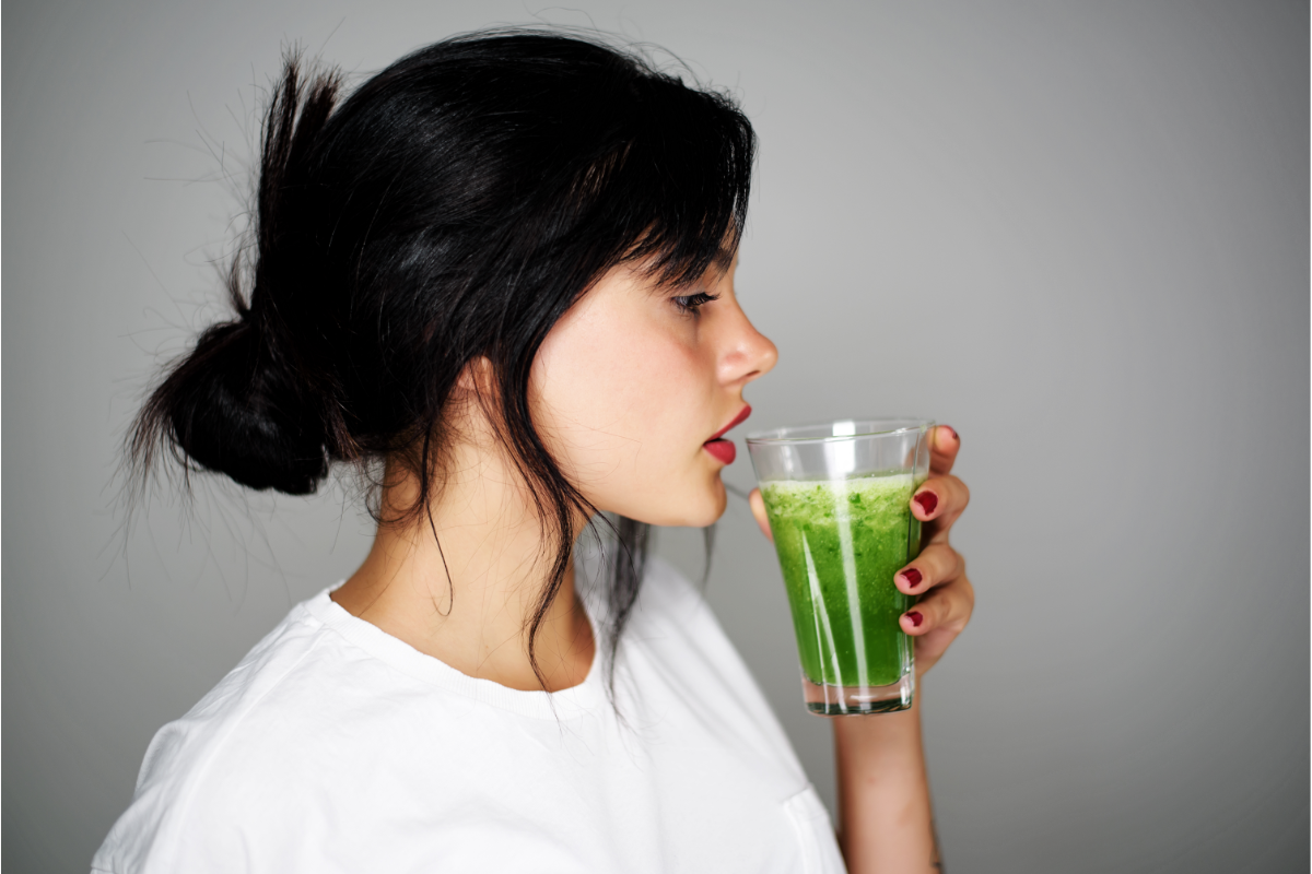 Femme buvant un smoothie vert riche en antioxydants pour la détoxification naturelle des métaux lourds tels que le plomb et le cadmium, favorisant l'élimination des toxines grâce à des solutions diététiques naturelles et des aliments détoxifiants comme la spiruline et la coriandre.