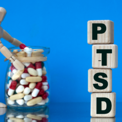 Blocs de bois avec l'acronyme PTSD et un mannequin manipulant des pilules, représentant les traitements médicamenteux et les alternatives naturelles pour le trouble de stress post-traumatique.