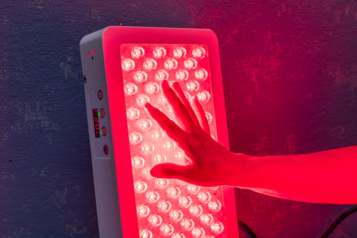 Main exposée à une lampe de luminothérapie LED rouge, utilisée pour améliorer la peau, stimuler le collagène et favoriser la régénération cellulaire.
