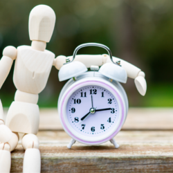 Un mannequin en bois pose son bras sur un réveil matin, illustrant le concept des rythmes circadiens et de l’horloge biologique.